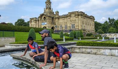 People looking into a pond outside a large manor house