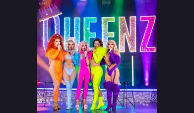 A picture of Queenz, on stage and wearing brightly-coloured outfits